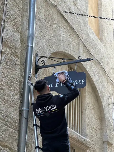 Nettoyage d'une enseigne drapeau suspendue sur une façade en pierre