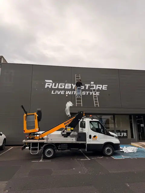 Camion nacelle devant une enseigne de magasin en lettres découpées