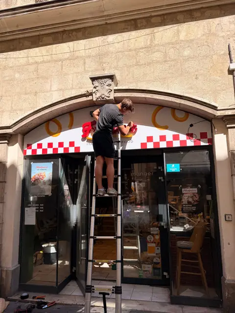 Poseur fixant des lettres boîtier lumineuses sur l'enseigne d'un restaurant à Montpellier